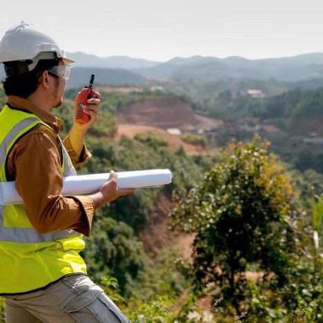 Engineer manager man with white helmet and hold construction paper plan use fm handheld transceiver or walkie talkie to communicate with his team.